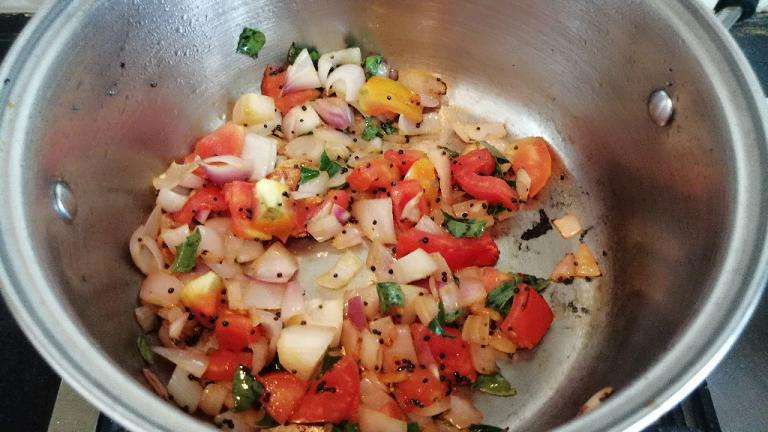 Take a pan and add in oil, mustard seeds, onions, tomatoes and curry leaves.