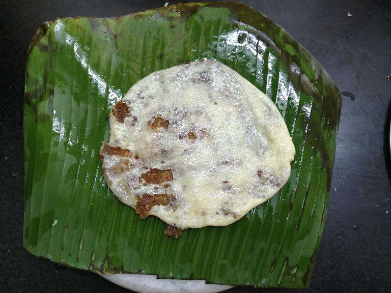 Take a piece of banana leaf, grease them with oil, and take a dough and place the coconut filling at the center then cover it and flatten them.