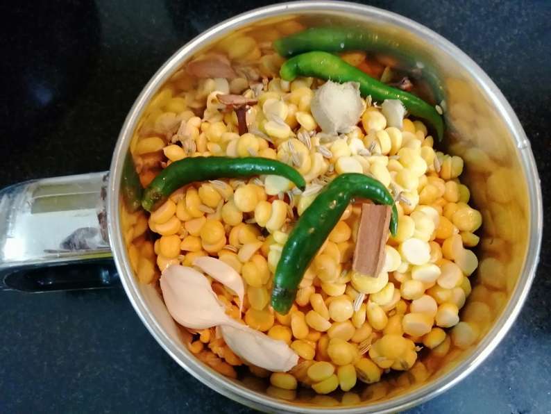 Take a mixer jar and add in soaked, drained channa dal, green chilies, garlic, ginger, cloves, cinnamon fennel seeds. Grind them coarsely. 