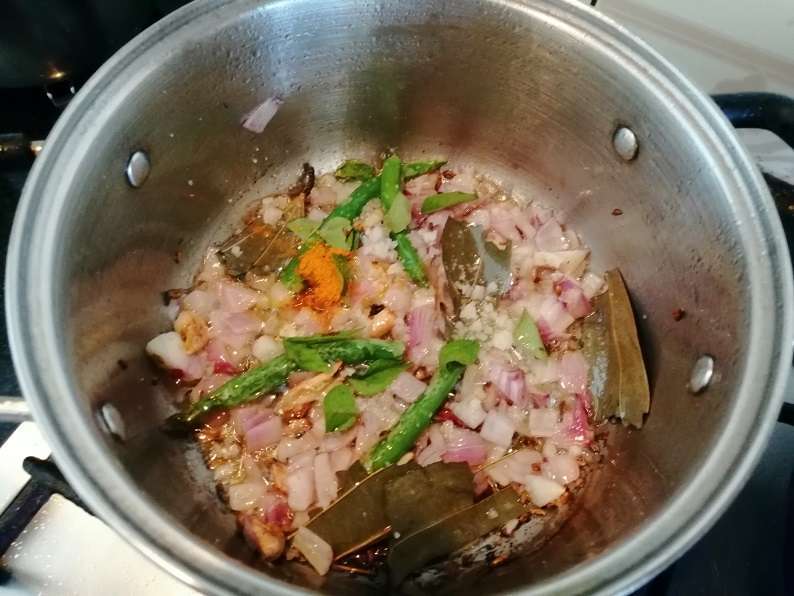 Heat a pan and add in oil, bay leaf, cloves, cinnamon stick, cardamom, crushed garlic, green chilies, chopped onion, turmeric powder, hing.