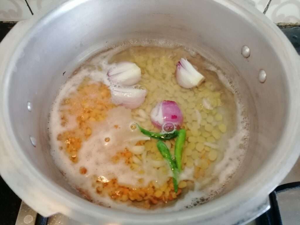 Heat a pressure cooker and add in water avarebele, toor dal and moong dal, onion, green chilies, garlic pods.