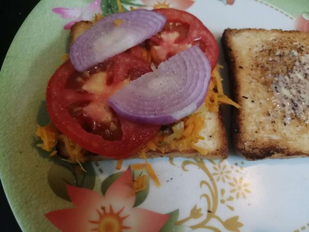 Add in sliced onions, tomatoes and sprinkle some salt and pepper on it and finally cover it with one more bread and serve.